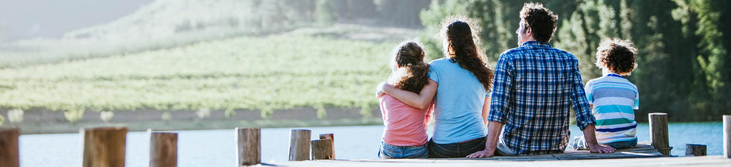 Familie sitzt am Steg eines Sees und genießt ihren Sommerurlaub 2021