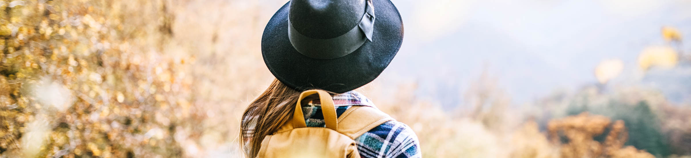 Junge Frau mit Hut und Rucksack wandert in herbstlicher Umgebung