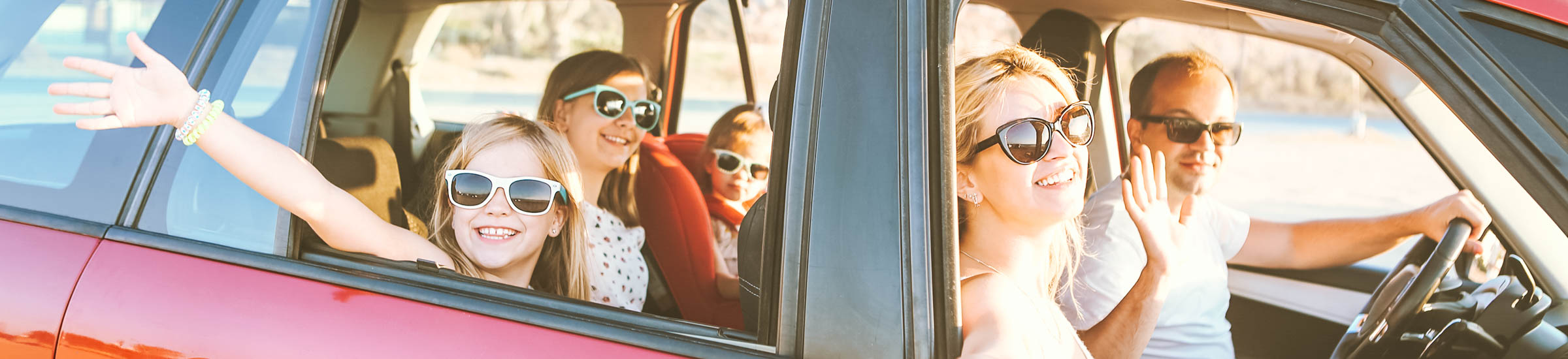 Familie mit drei Kindern winkt in die Kamera – Lange Autofahrt mit Kindern