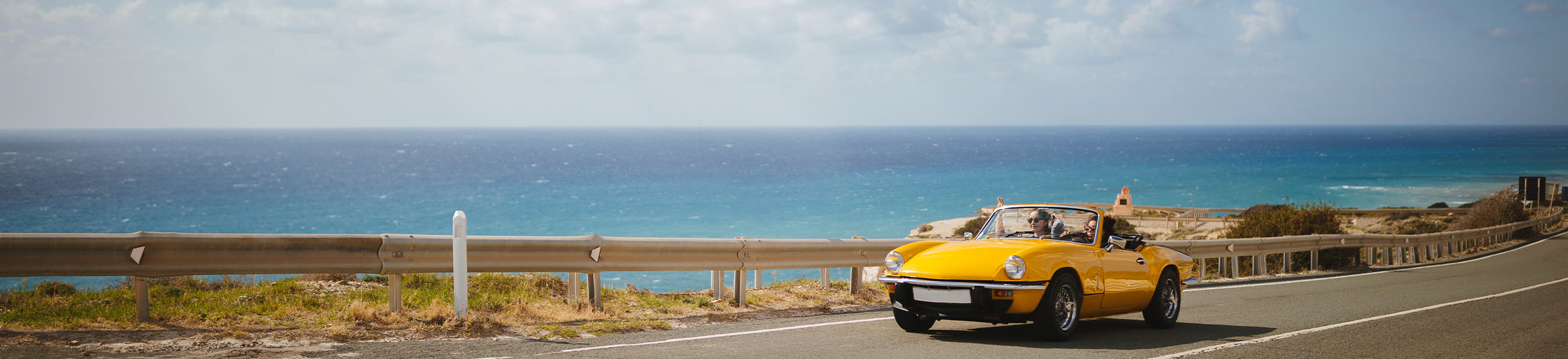 Frau fährt im gelben Cabrio an der Küste entlang