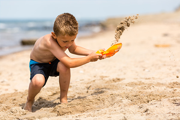 Junge mit Strandspielzeug im Sand