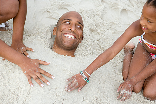 Mann wird von Kindern im Sand eingebuddelt