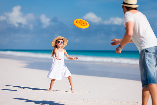 Mädchen und Vater spielen Frisbee am Strand