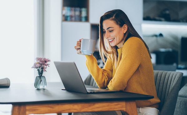 Eine junge Frau sitzt am Laptop und hat eiine Tasse in der Hand