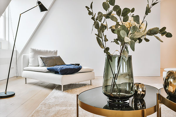 Moderne Dekoration mit einer grünen Vase, Eukalyptus-Zweigen auf einem Tisch und eine Stehlampe nehmen einem Sessel - passend zur modernen Einrichtung