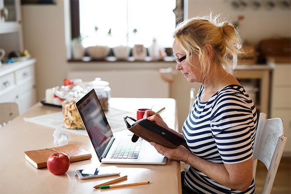 Ältere Frau, die am Laptop sitzt und eine Buchung in Ihren Kalender einträgt