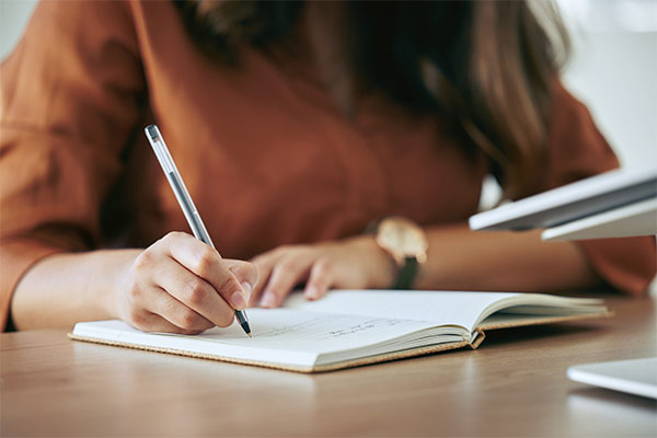 Frau, die mit Notizbuch am Schreibtisch sitzt. um Namen für ihre Ferienunterkunft zu brainstormen