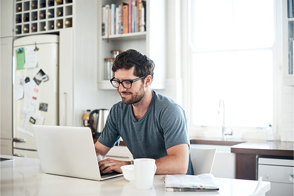 Mann der in seiner Küche vorm Laptop sitzt und Mails beantwortet