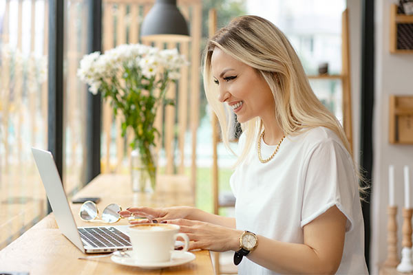 Junge Frau, die während einer Workation am Laptop sitzt repräsentiert die Zielgruppe der Geschäftsreisenden